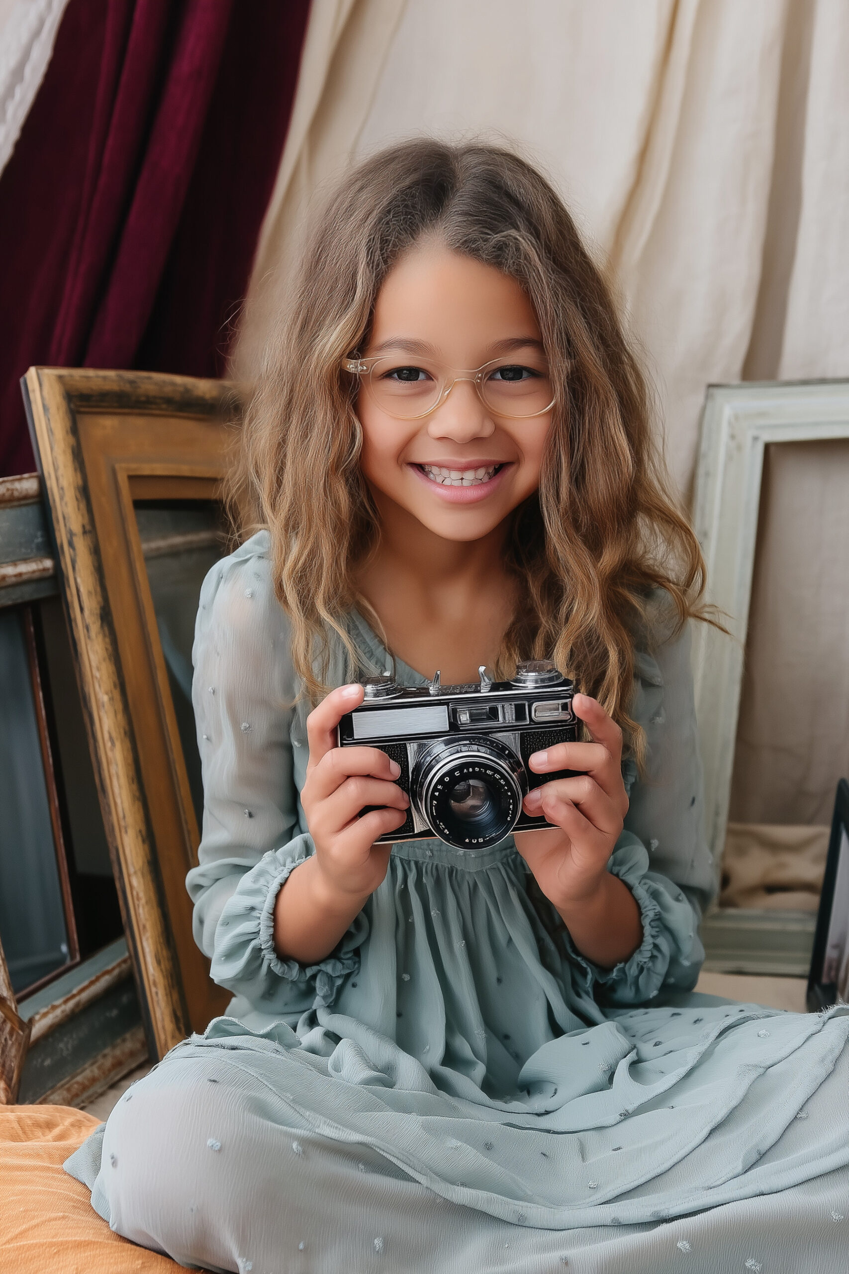 Kindergarten Fotoset mit einem dunkelhaarigen Mädechen, das einen Retro-Fotoapparat in den Händen hält und in die Kamera lächelt.
